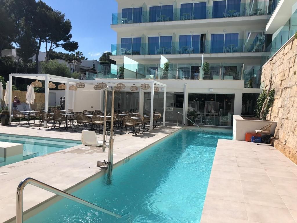 Moderner Poolbereich im BQ Paguera Boutique Hotel mit schmalem Pool, Sonnenterrasse, Rattanmöbeln und Glasbalkonen vor einem mehrstöckigen Gebäude.