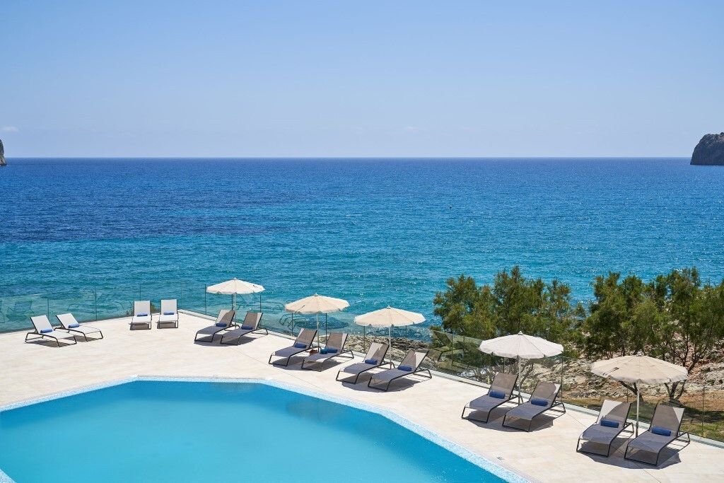 Infinity-Pool des Bahía Suites Camp de Mar mit Panoramablick auf das türkisfarbene Mittelmeer, umgeben von Sonnenliegen und Sonnenschirmen auf einer Terrasse mit Glasbrüstung.