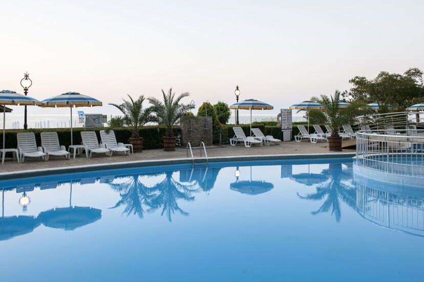Ruhiger Poolbereich des GRIFID Encanto Beach Hotels mit Liegestühlen, Palmen und Sonnenschirmen vor der Kulisse des Meeres in der Abendstimmung.