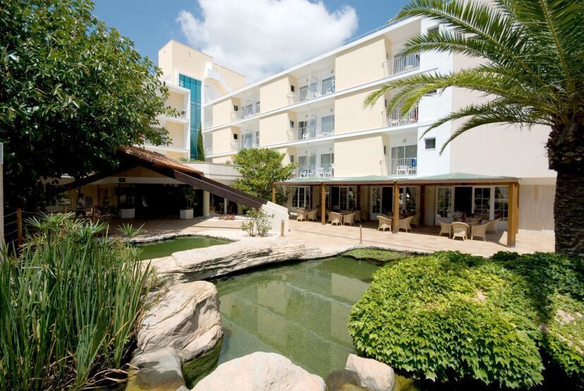 Das Hotel Capricho & Spa auf Mallorca bietet eine grüne Oase mit Teich, Palmen und überdachter Terrasse – ideal zum Entspannen in mediterraner Atmosphäre.