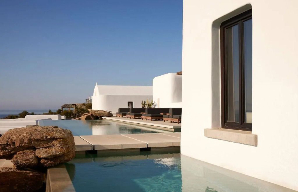 Luxuriöser Poolbereich im Kalesma Mykonos mit minimalistischer Kykladen-Architektur, weißen Fassaden, Felsdeko und Blick aufs Meer – stilvolle Ruheoase mit exklusivem Design.
