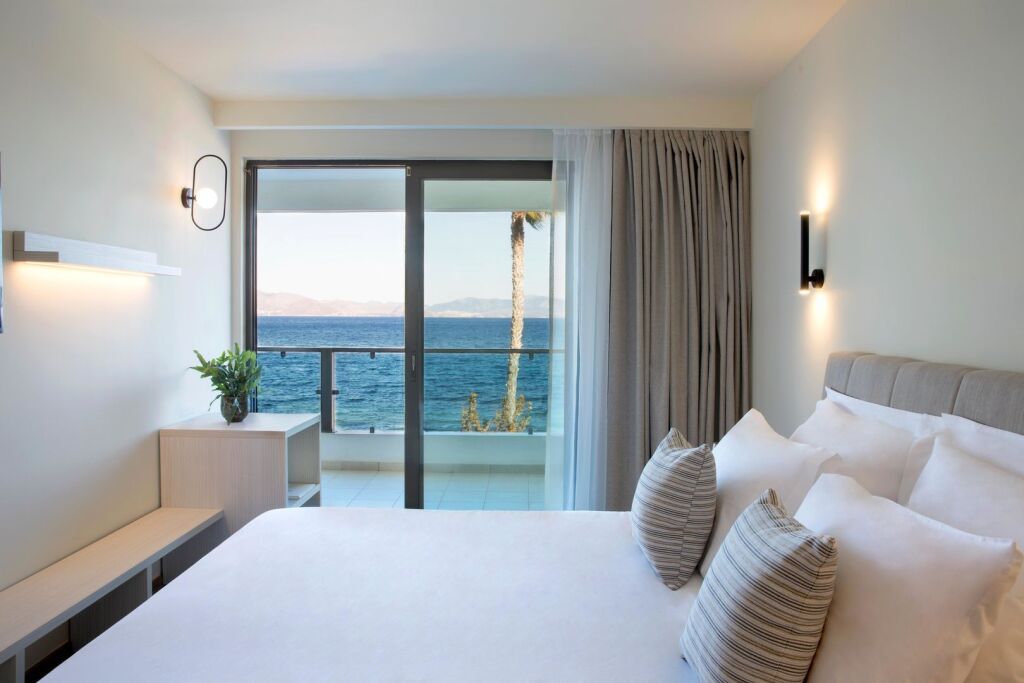 Helles, modern eingerichtetes Hotelzimmer mit gemütlichem Bett, minimalistischer Deko und Balkon mit traumhaftem Blick auf das Meer – Teil des Kosea Boutique Hotels auf der Insel Kos.