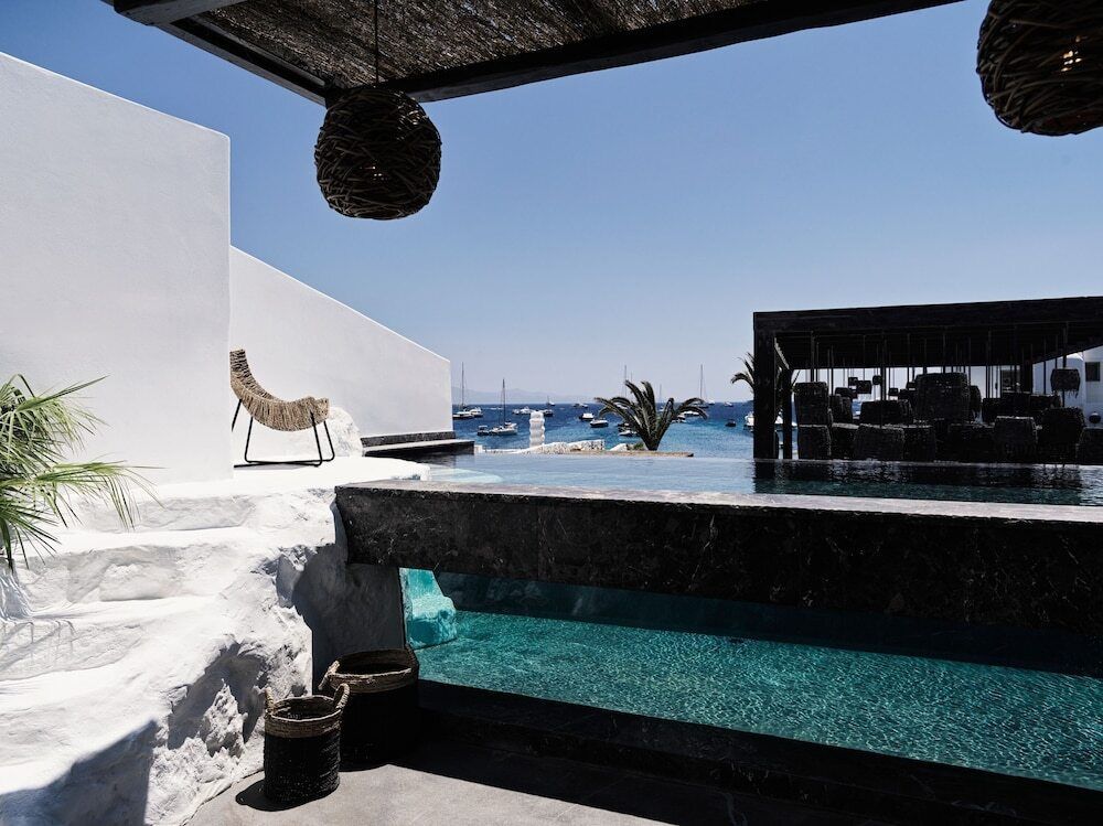 leganter Poolbereich im Myconian O Mykonos mit stylischem Design, weißen Wänden, schwarzem Naturstein, Blick auf das Meer und entspannter Lounge-Atmosphäre mit modernen Akzenten.