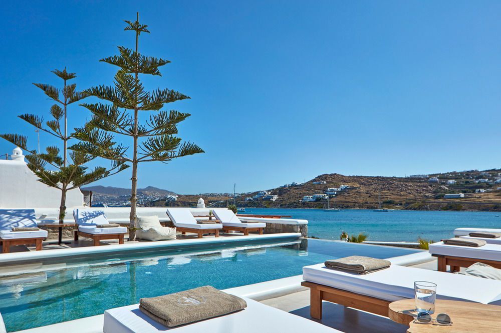 Eleganter Poolbereich mit weißen Sonnenliegen, türkisfarbenem Wasser und Meerblick – Mykonos Waves Beach House and Suites mit entspannter Atmosphäre direkt an der Küste.