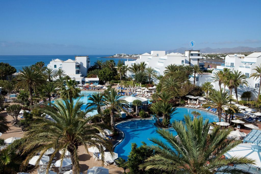 Blick auf das Seaside Los Jameos Resort auf Lanzarote mit üppigen Palmen, großen Poollandschaften und weißer Architektur direkt an der Küste.