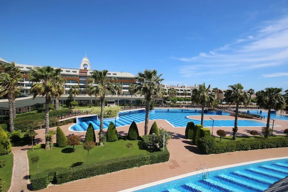 Vor dem TUI MAGIC LIFE Jacaranda erstreckt sich eine weitläufige Poollandschaft mit geometrischen Formen, eingerahmt von Palmen und gepflegtem Grün.