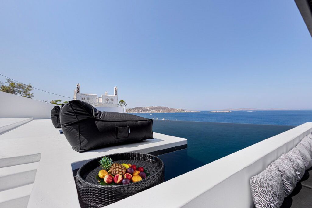 Infinity-Pool mit Meerblick, schwarzen Loungesesseln und Obstschale auf weißer Terrasse – stilvolle, minimalistische Atmosphäre im Tagoo Black Hotel auf Mykonos.