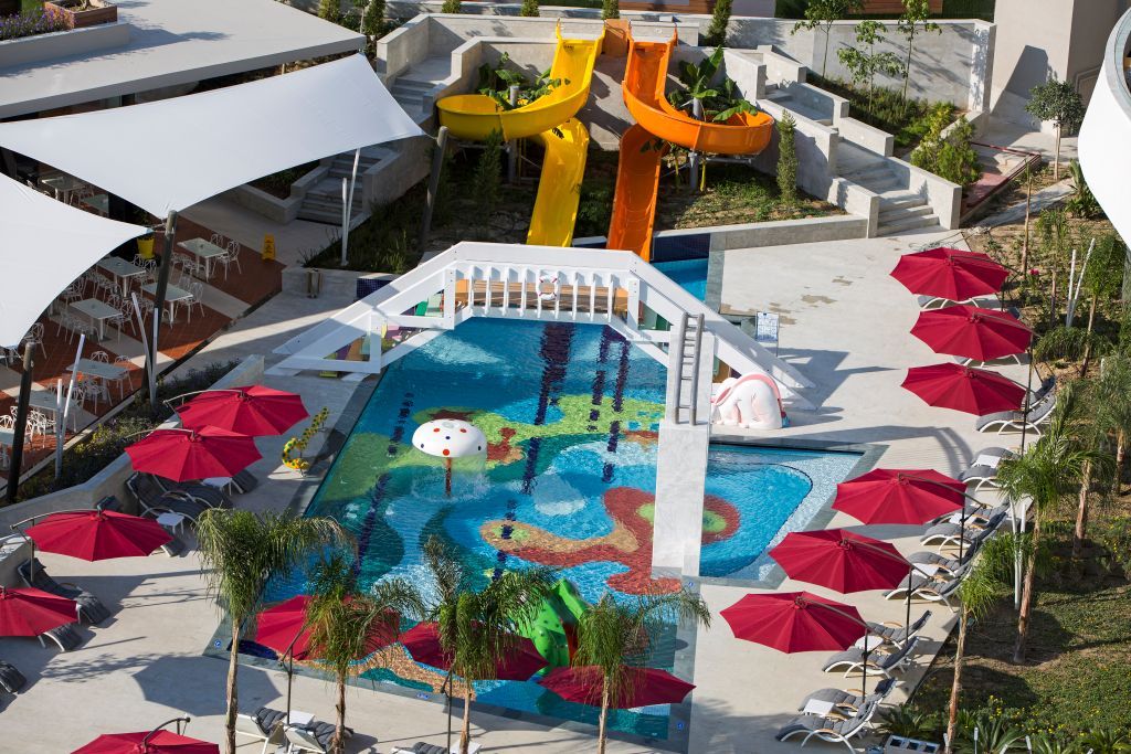 Der Kinderpool des The Sense De Luxe Hotel ist mit bunten Wasserrutschen, Spielgeräten und roten Sonnenschirmen ausgestattet.