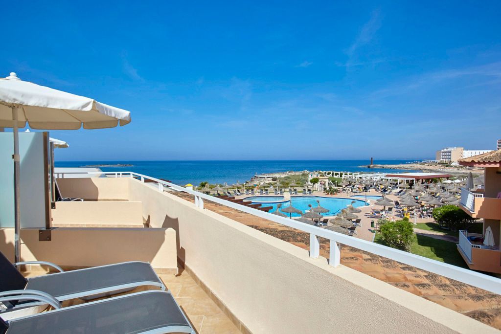 Blick von der Sonnenterrasse des Universal Grand León & Spa auf den Hotelpool und das tiefblaue Mittelmeer mit Liegen, Sonnenschirmen und einer weitläufigen Poollandschaft.