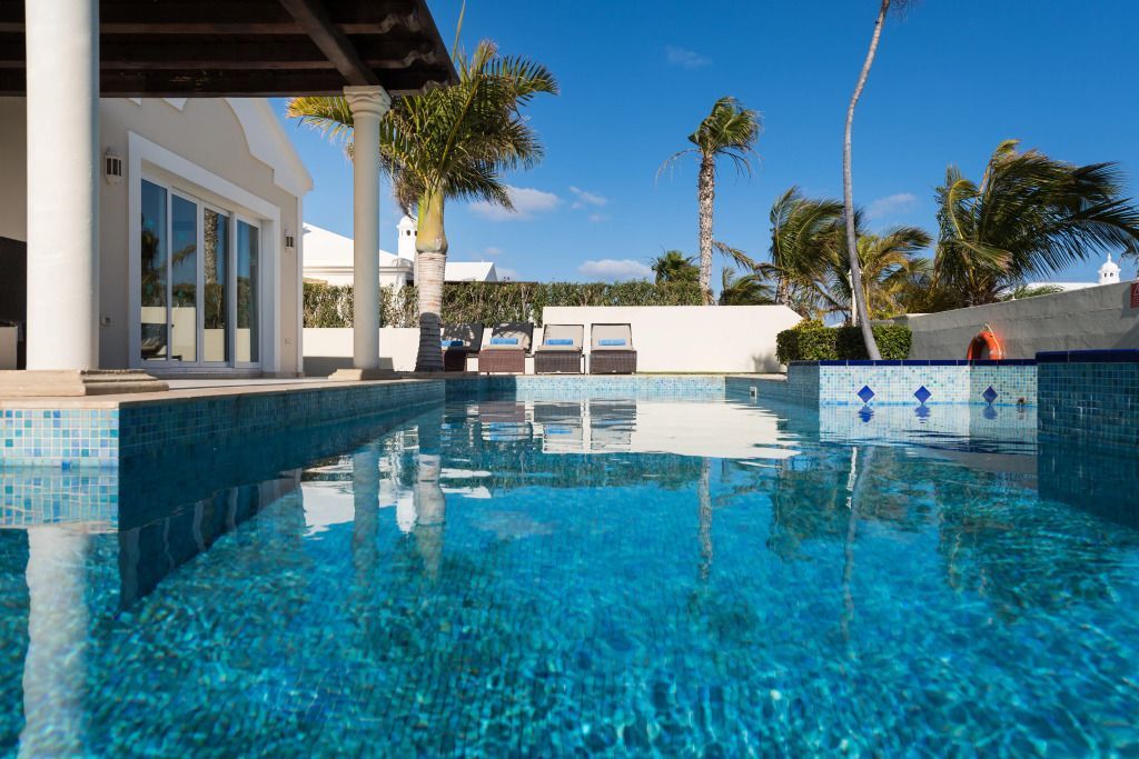 Private Villa der Villas Alondra auf Lanzarote mit überdachter Terrasse, direktem Zugang zum Pool, Palmen und klarblauem Himmel.