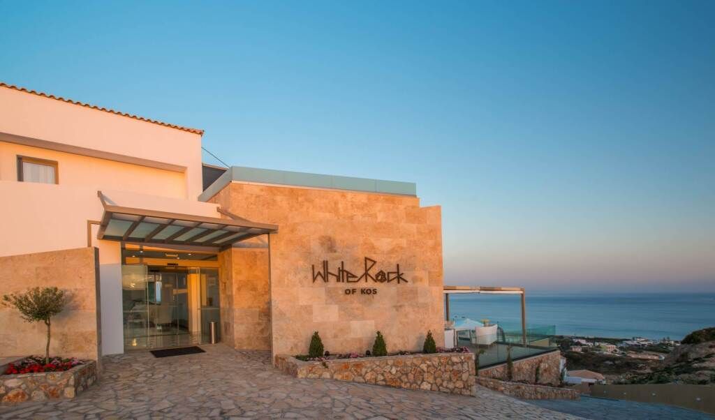 Eingangsbereich des White Rock of Kos – Adults Only: modernes Hotel mit Natursteinfassade, klaren Linien und atemberaubendem Blick auf das Meer bei Sonnenuntergang.