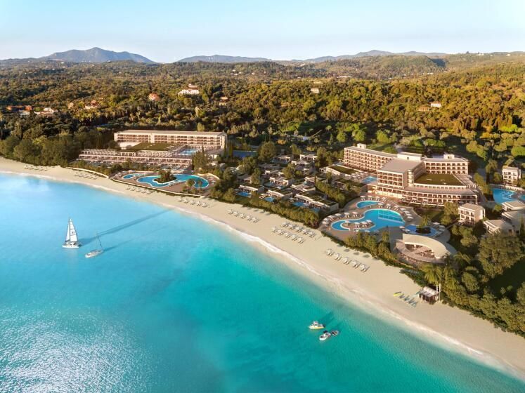 Luftaufnahme des Ikos Dassia Resorts auf Korfu mit direkter Strandlage, türkisfarbenem Wasser, mehreren Pools und Gebäudekomplexen, eingebettet in eine grüne Hügellandschaft.