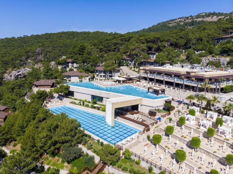 Modernes Hotelresort mit spektakulärem, auf zwei Ebenen gebautem Poolkomplex in Hanglage, umgeben von grüner Pinienlandschaft und Blick auf das Meer.