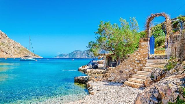 Kleine Bucht mit türkisem Wasser, Steintreppe und Segelboot in der Ägäis