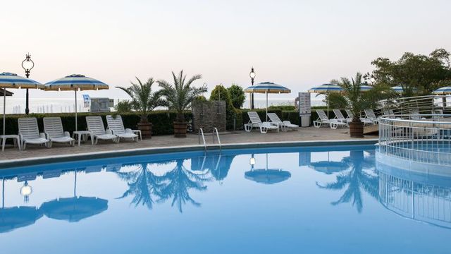 Ruhiger Poolbereich des GRIFID Encanto Beach Hotels mit Liegestühlen, Palmen und Sonnenschirmen vor der Kulisse des Meeres in der Abendstimmung.